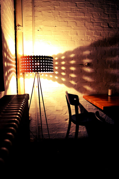 Stehleuchte Midi mit bronzefarbenen Nespresso-Kapseln wirft warmes Lichtmuster an eine Backsteinwand